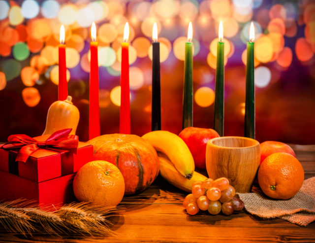 Kwanzaa+holiday+concept+with+decorate+seven+candles+red%2C+black+and+green%2C+gift+box%2C+pumpkin%2C+bowl+and+fruit+on+light+blur+bokeh+background